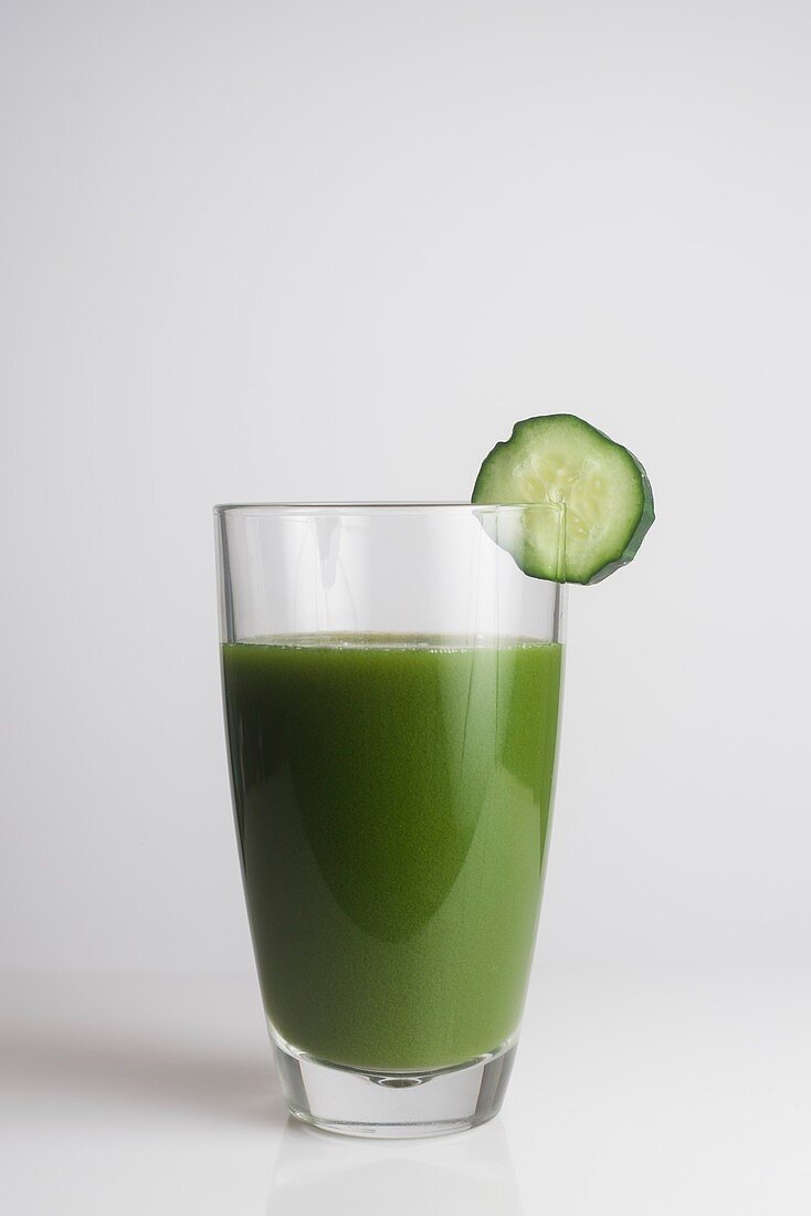A glass of fresh green juice with a slice of cucumber