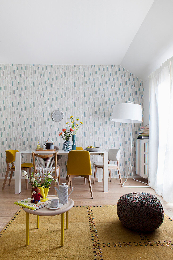 View past coffee table and pouffe into dining area with floral wallpaper