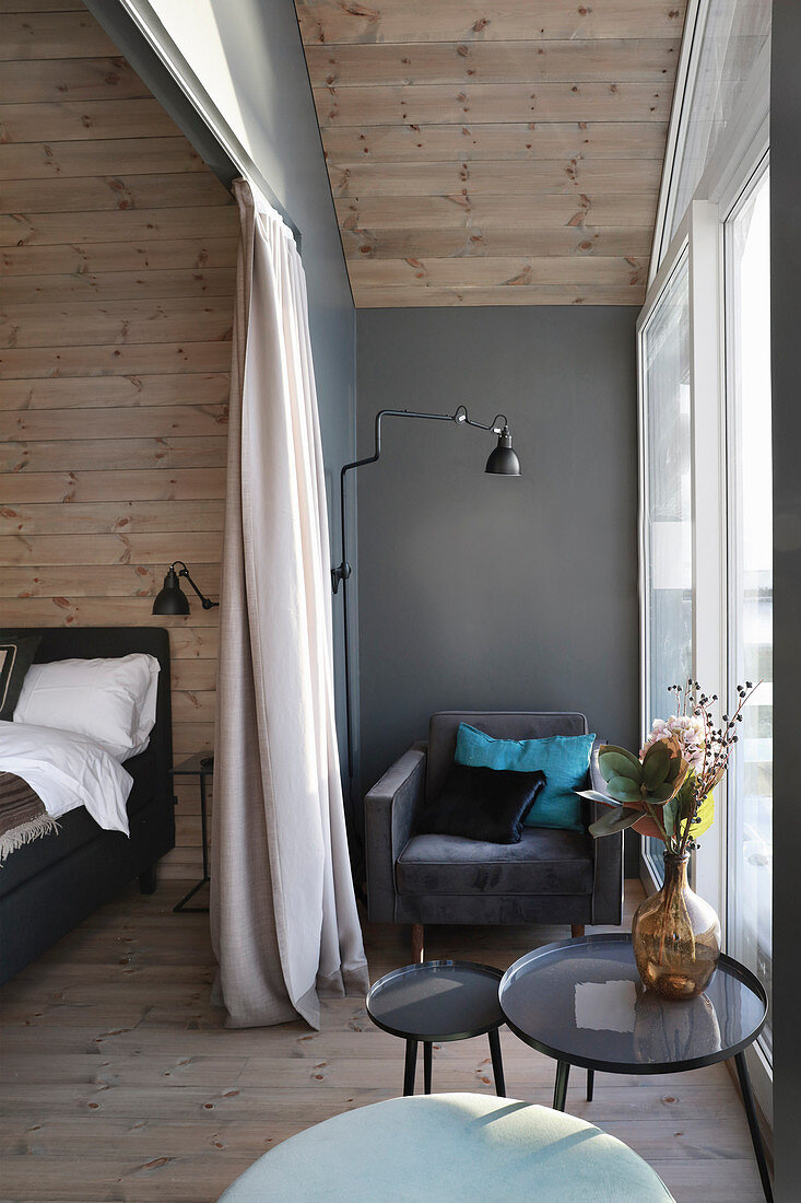 Armchair next to window in elegant bedroom with wood-clad walls