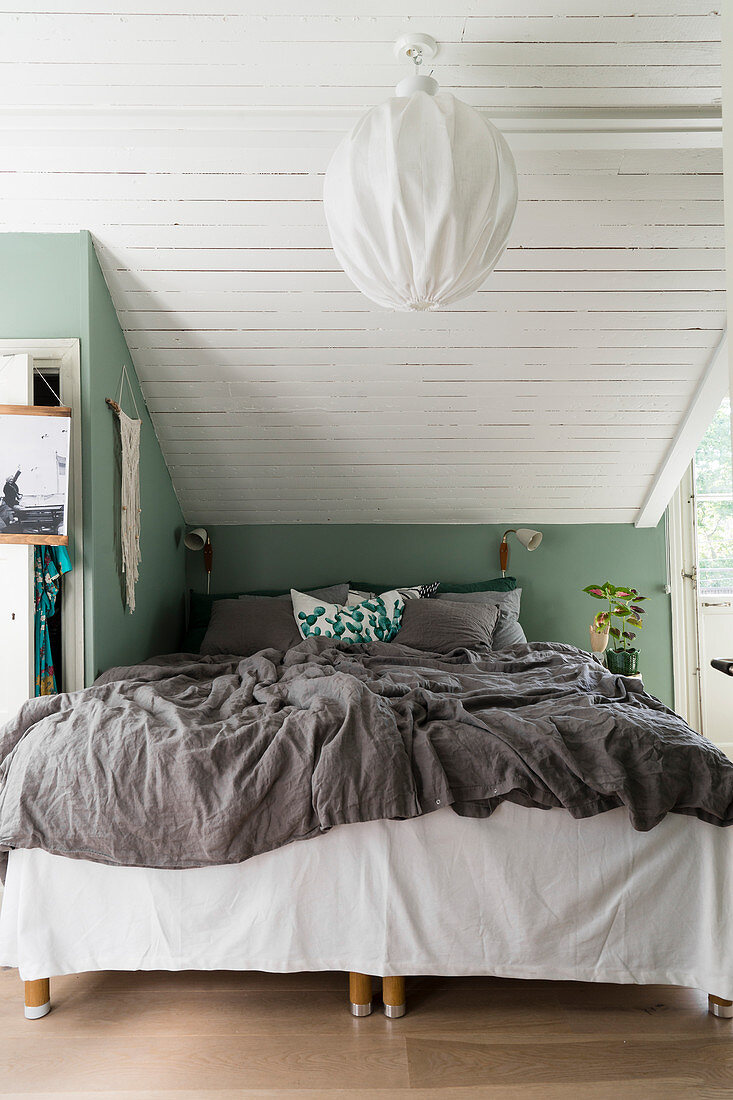 Bed below sloping ceiling with green knee wall and wood-clad ceiling
