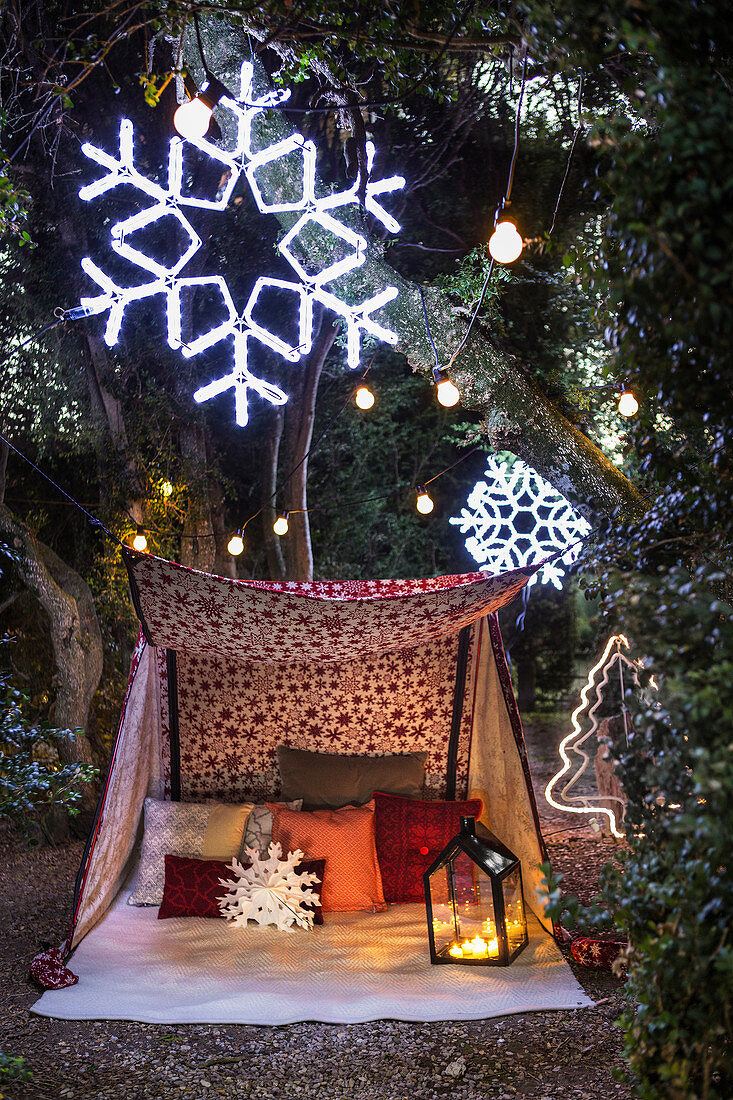 Cushions and lanterns in tent in garden decorated with snowflakes and fairy lights