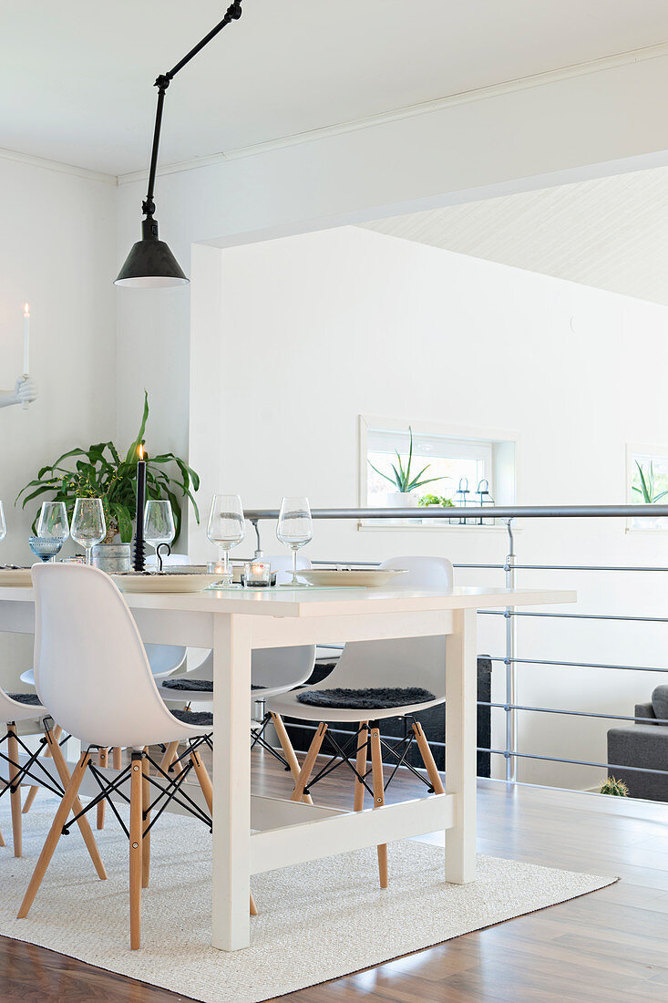 Shell chairs around white dining table next to balustrade of gallery above living space