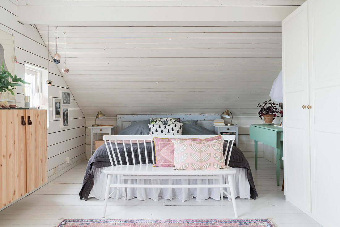 Spoke-back bench at foot of bed with valance below sloping ceiling in bedroom