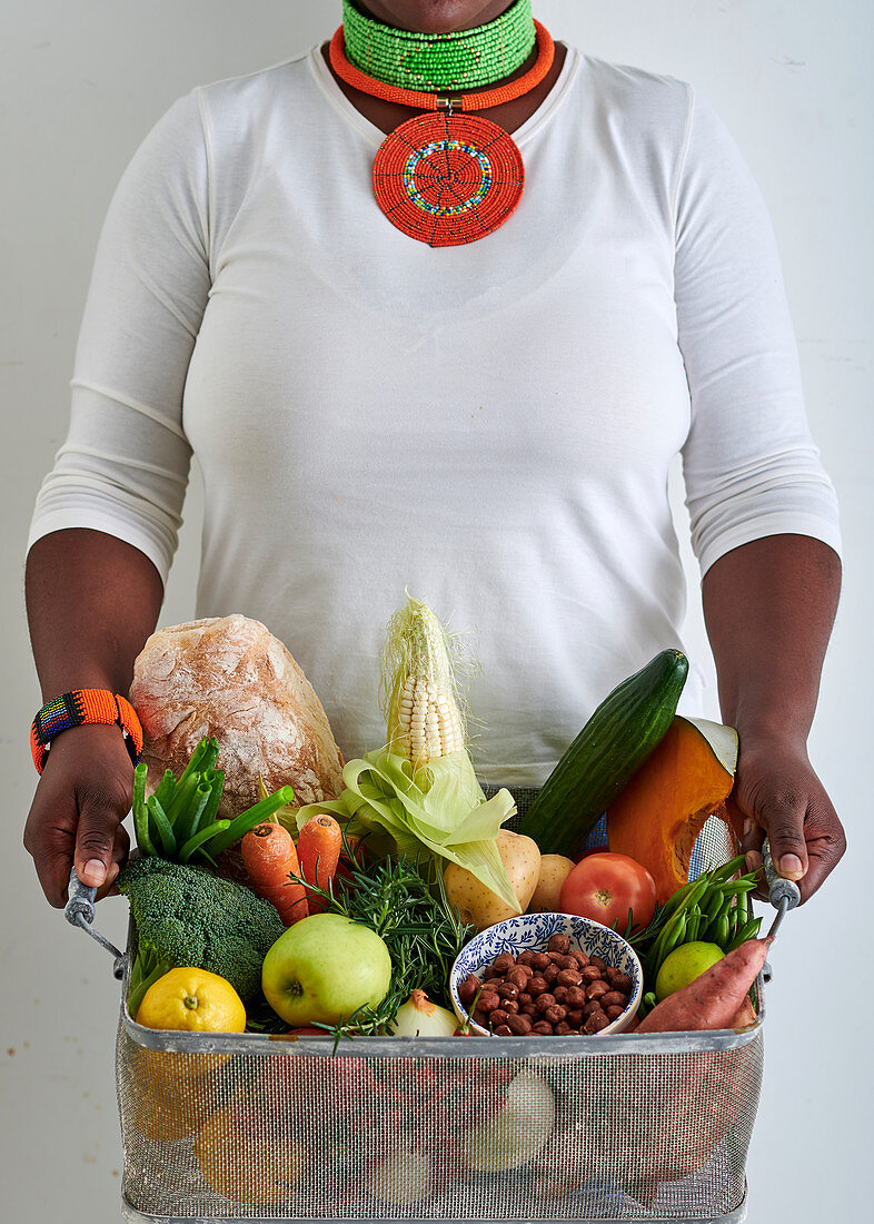 A woman holding a basket with vegetables, fruit and food