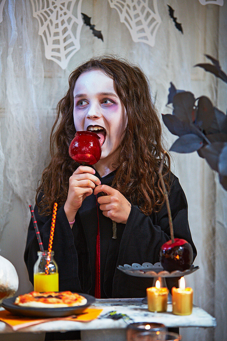 Verkleidetes Mädchen isst Karamellapfel zu Halloween