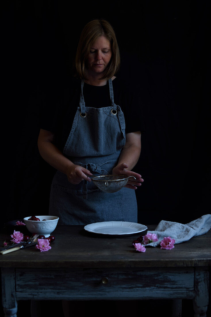 A woman sieves icing sugar over a cake plate