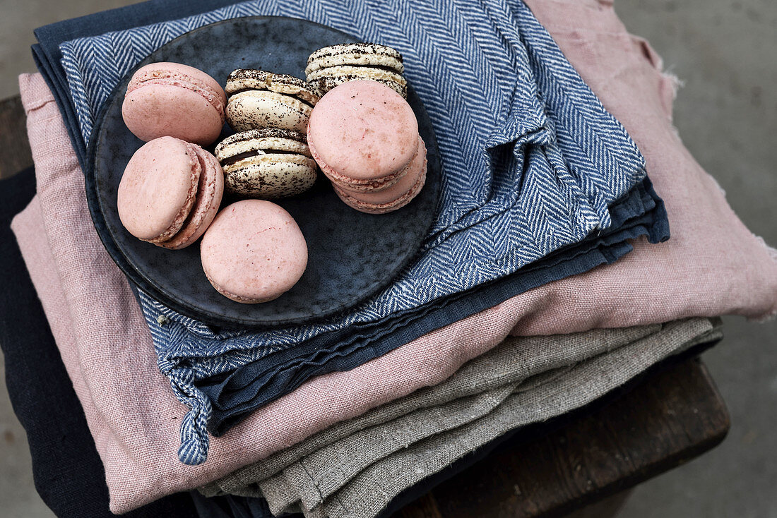 Zweierlei Macarons auf Teller und gestapelten Tischtüchern