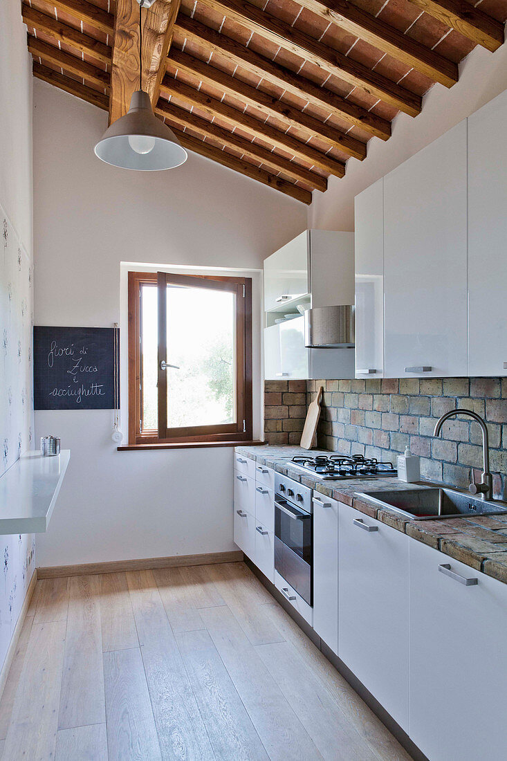 Küche in toskanischem Landhaus mit weißen Küchenfronten und Holzdeckenkonstruktion
