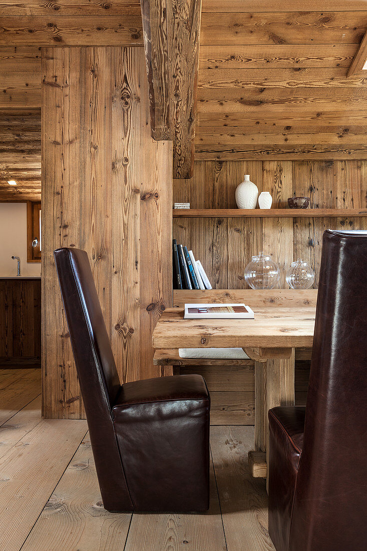 Dark leather chairs around dining table in modern wooden house