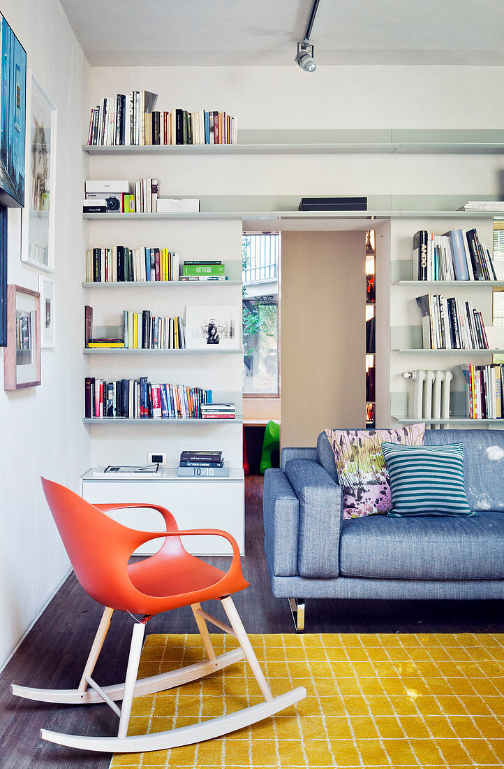 Couch and designer rocking chair in interior with floor-to-ceiling bookshelves