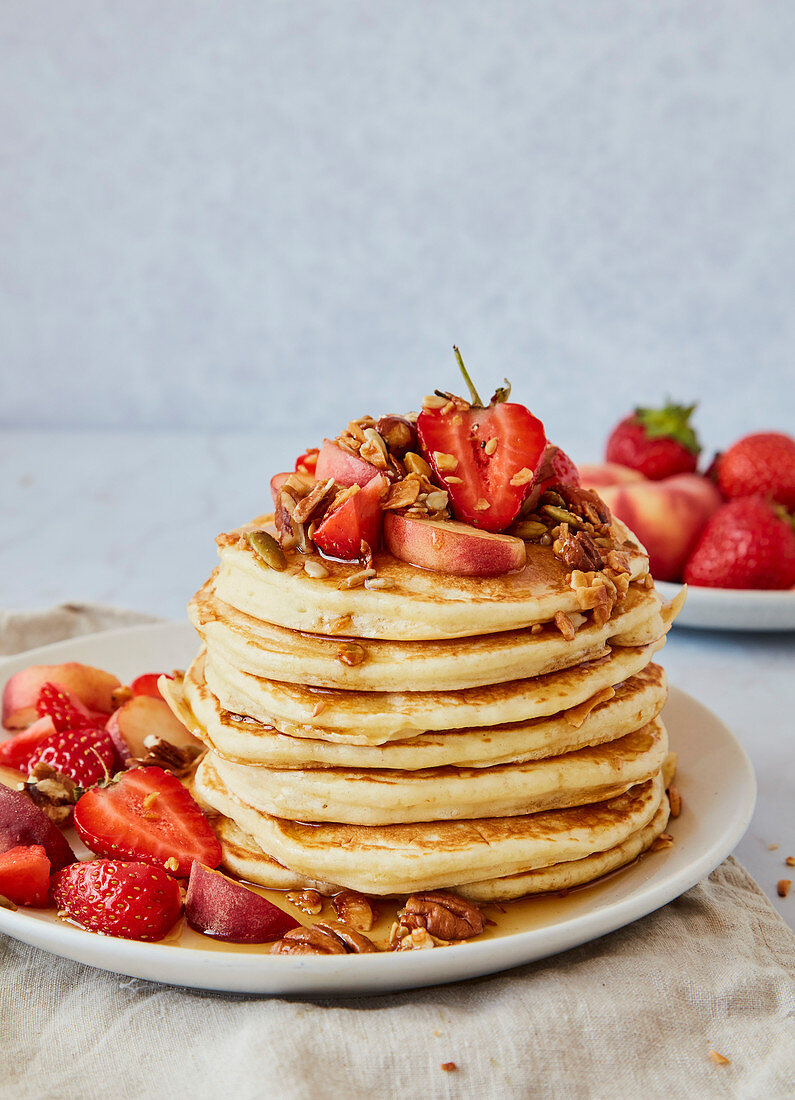 Ein Stapel Pancakes mit Erdbeeren, Pfirsichen, Granola und Ahornsirup