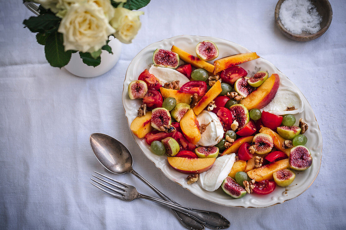 Peach, figs, grapes, cherry tomatoes, mozzarella and walnuts salad on a serving plate
