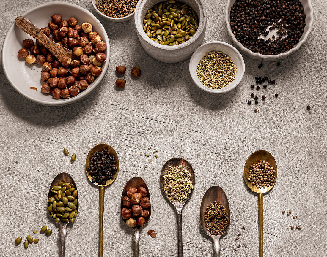 Assortment of spices, seeds and nuts in bowls on gray background
