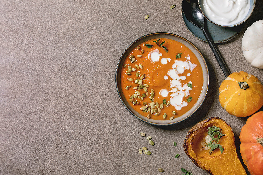 Pumpkin soup with cream and seeds in ceramic bowl, served with sour cream