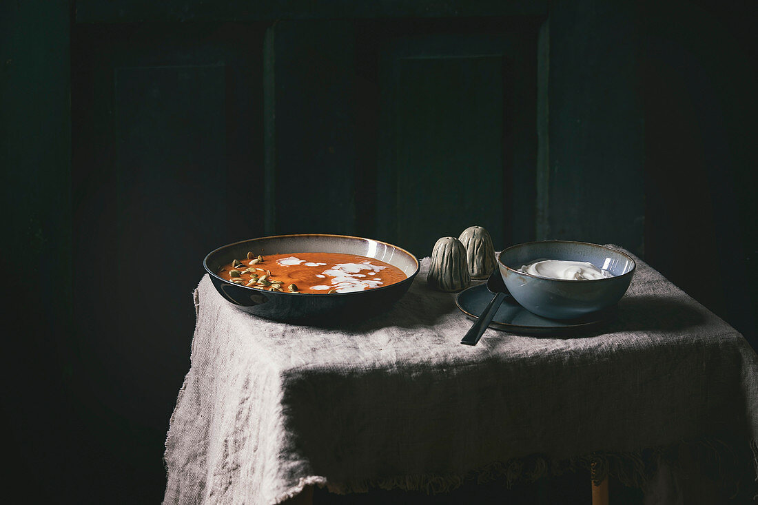 Kürbissuppe mit Sauerrahm und Kürbiskernen auf rustikalem Tisch