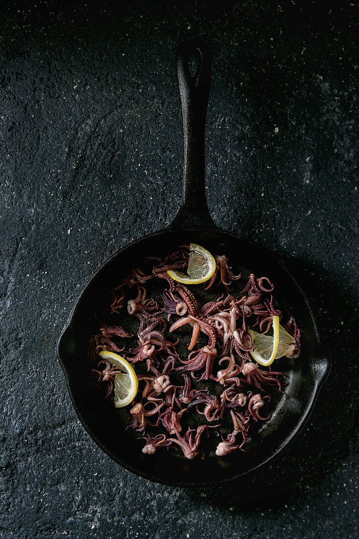 Grilled squids calamari tentacles with lemon in cast iron pan over black concrete background