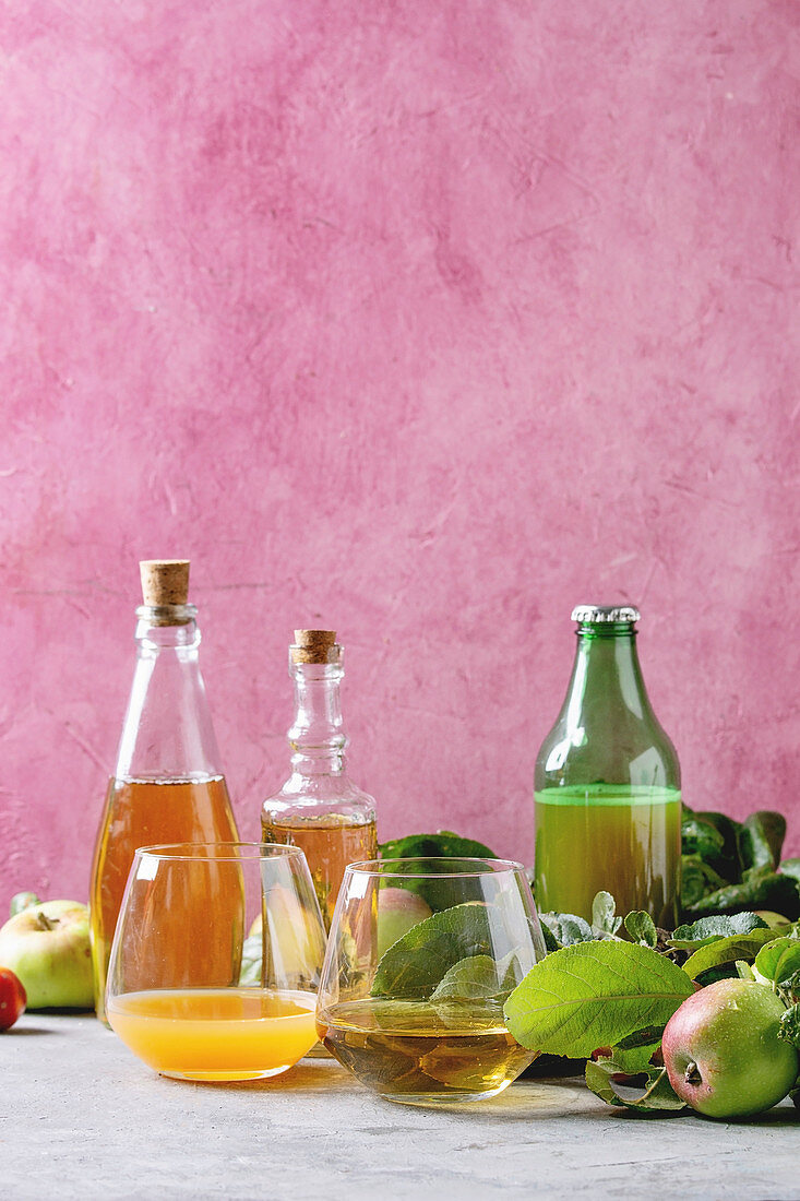 Apfelsaft, Apfelwein und Apfelessig vor pinkfarbenem Hintergrund