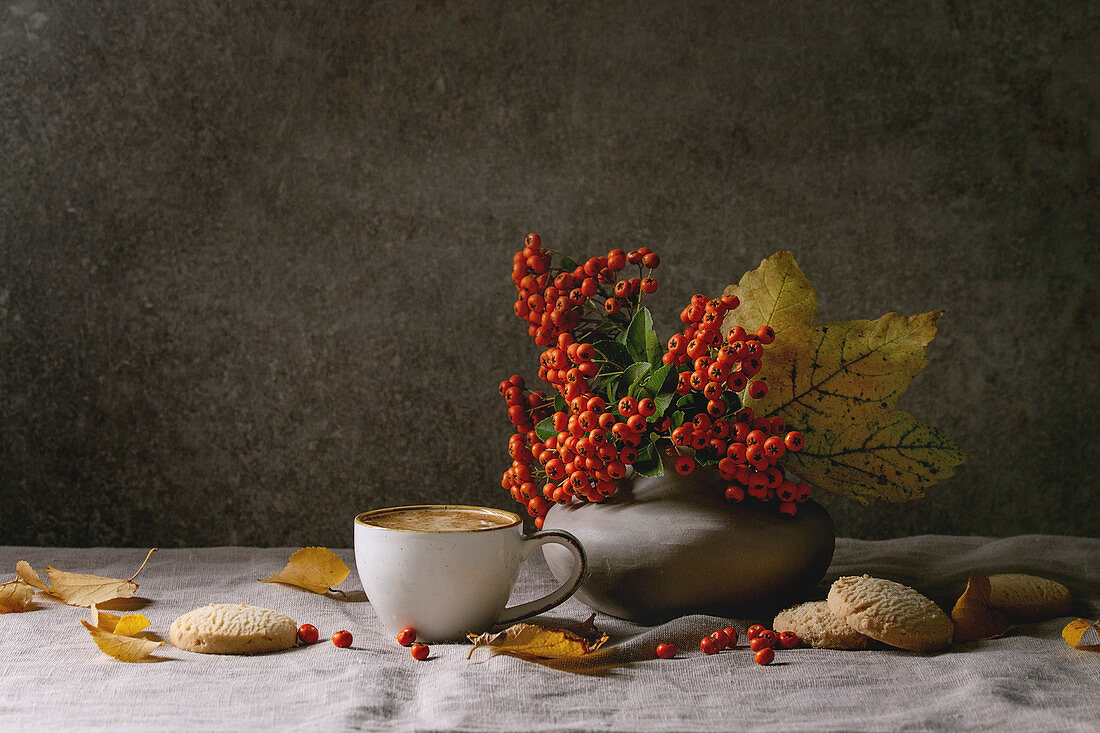 Cup of espresso coffee, autumn leaves, berries in ceramic vase, coffee beans and shortbread cookies
