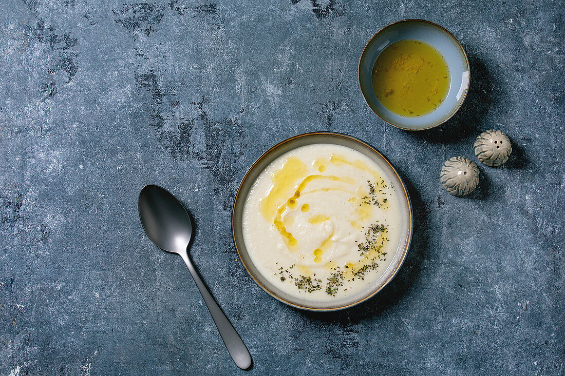 Parsnip or cauliflower cream soup in ceramic bowl with butter sauce and herbs