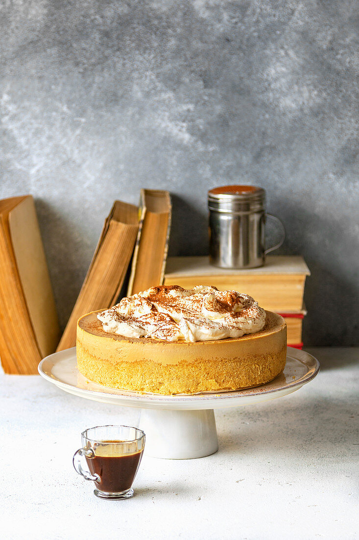 No bake cheesecake on a cake stand and a cup of coffee on the table