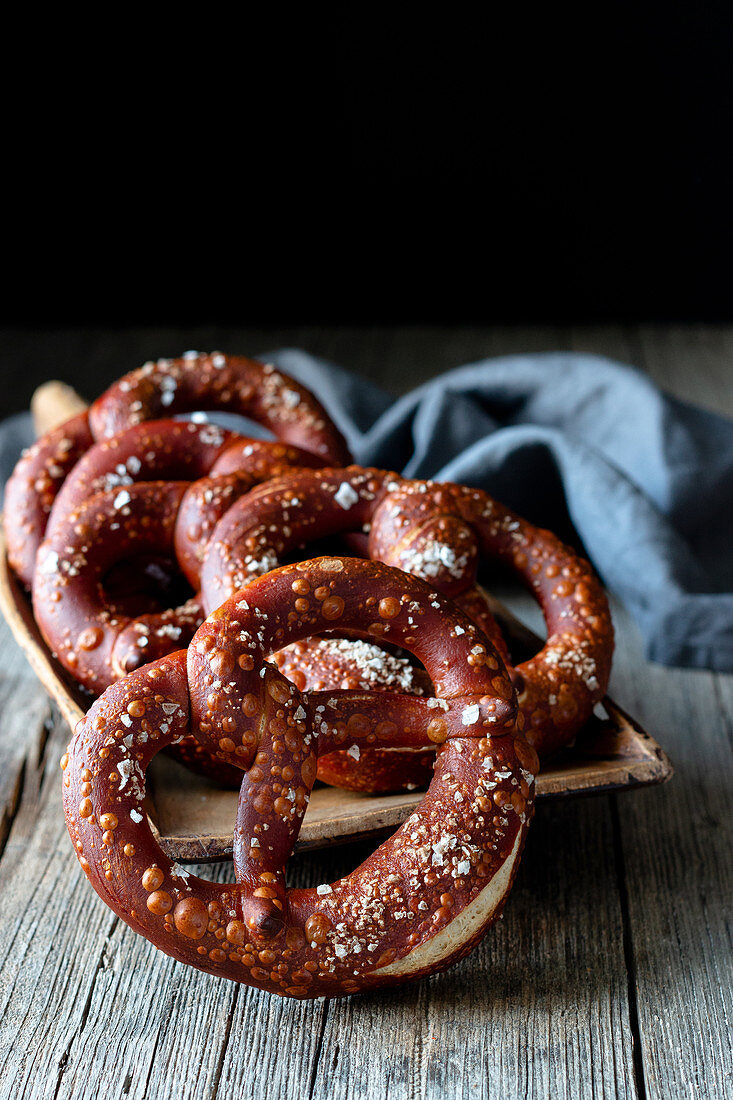 Fresh appetizing pretzels with salt arranged on scoop over old wooden surface
