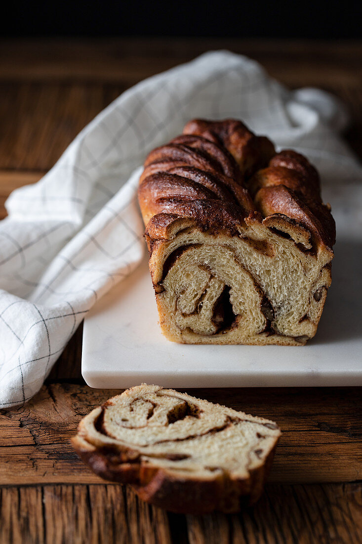 Fresh twisted bread or cinnamon babka over wooden table with striped towel on blurred background