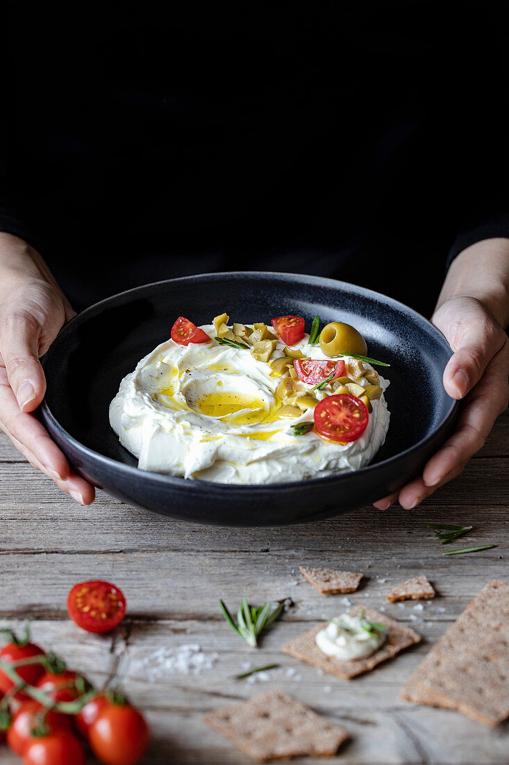 Crunchy crackers and rosemary and plate of labneh yogurt with tomatoes and olives