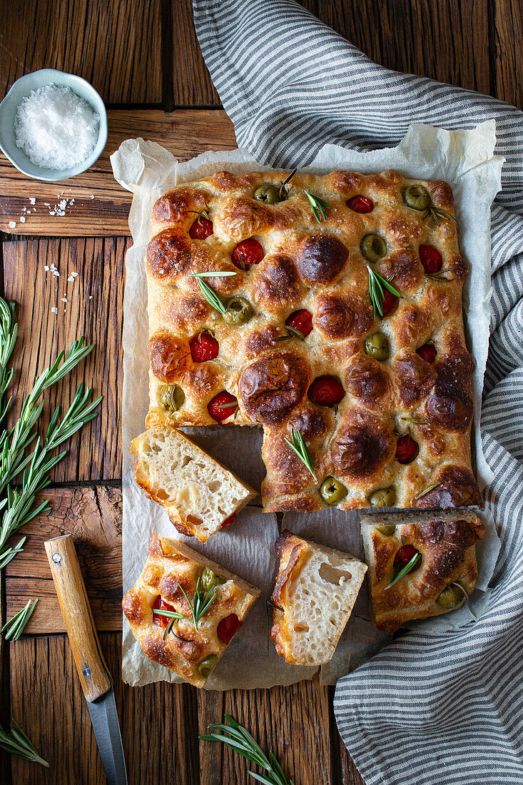 Overhead potato focaccia with fresh rosemary placed near bowl with salt and striped napkin on wooden table