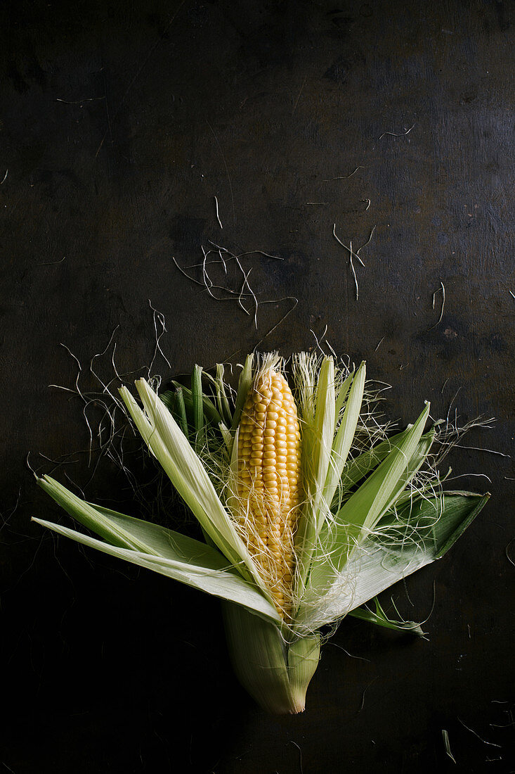 Top view of steps of fresh ripe corn peeling on black table