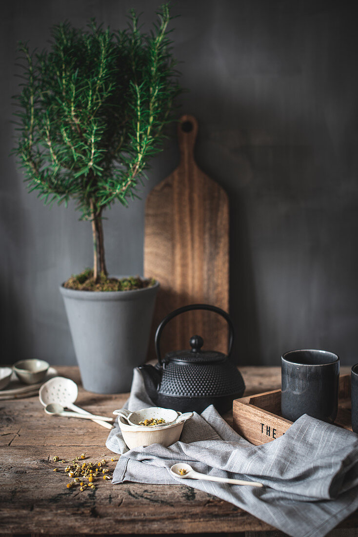 Composition of black teapot and white bowl and chamomile herbs on wooden table