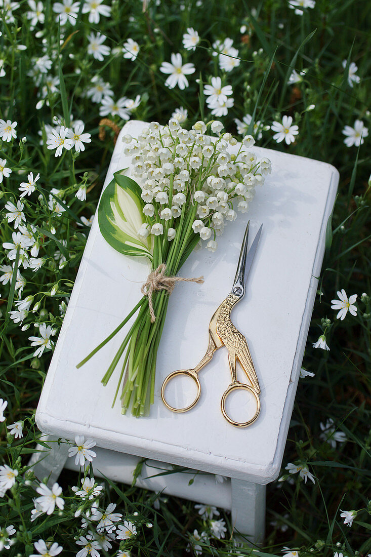 Posy of lily-of-the-valley and bird-shaped scissors on side table