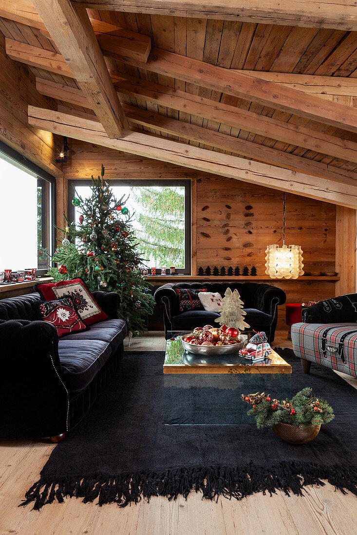Schwarze Polstermöbel und geschmückter Weihnachtsbaum im Wohnzimmer eines Chalets