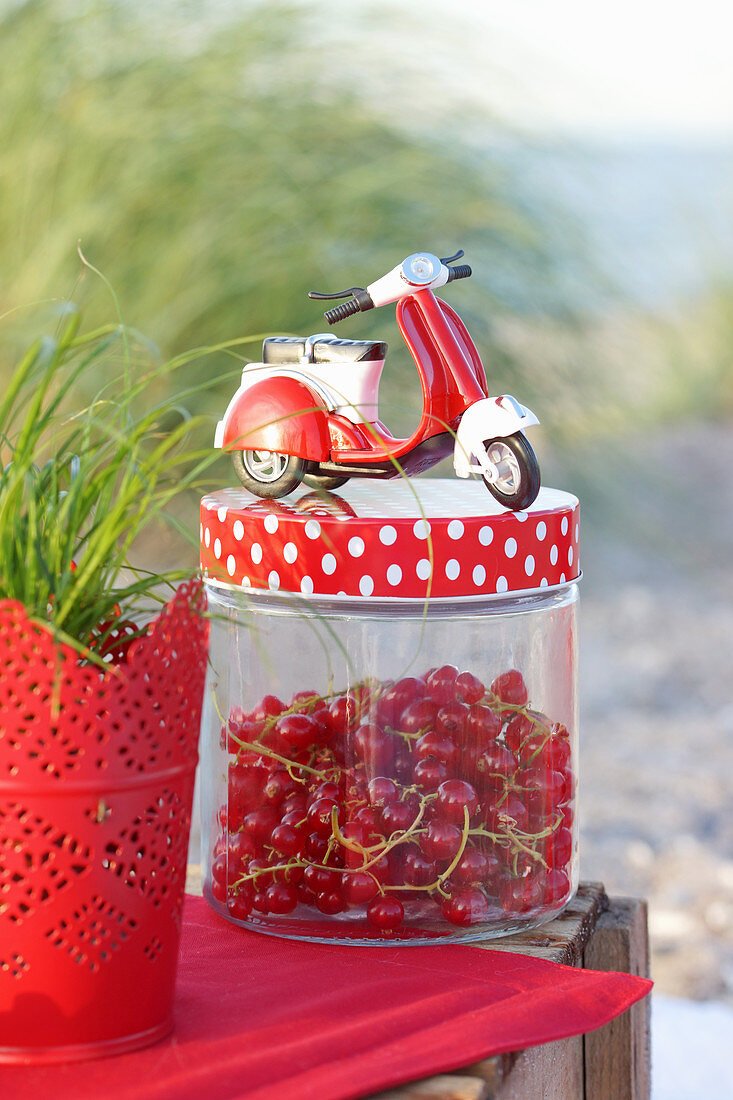 A Vespa model on top of a screw-top jar of redcurrants on a table on the beach