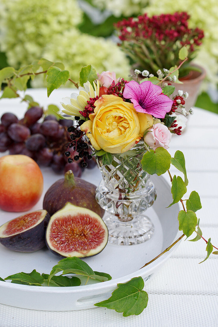 Fruit next to a bouquet of summer flowers in a vase on a table