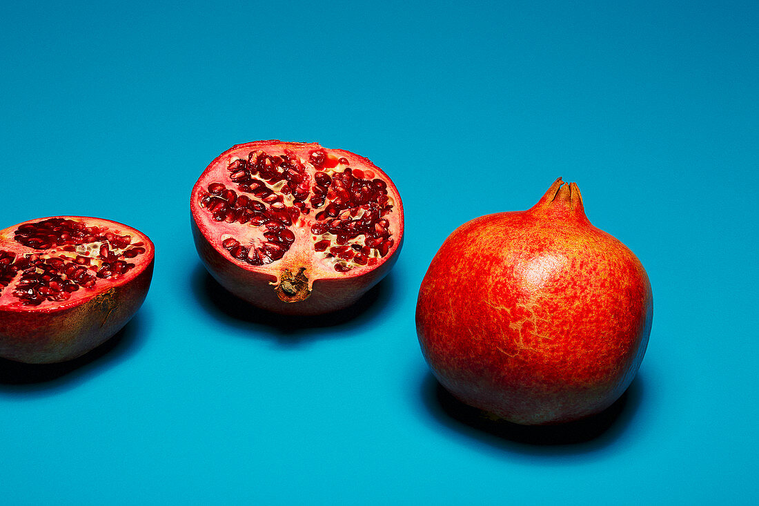 Whole and halved pomegranates in front of a blue background