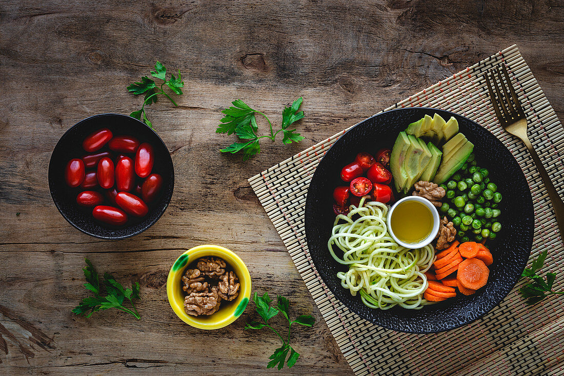 Zucchini raw vegan pasta with peas, cherry tomatoes and avocado