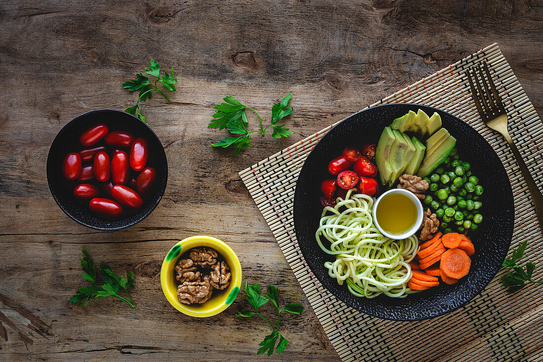 Zucchinispaghetti mit Erbsen, Kirschtomaten und Avocado in einer Schale