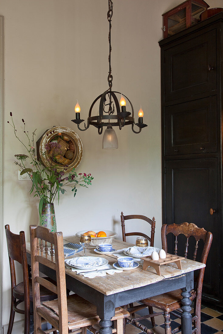 Rustic dining table and various chairs below wrought-iron chandelier