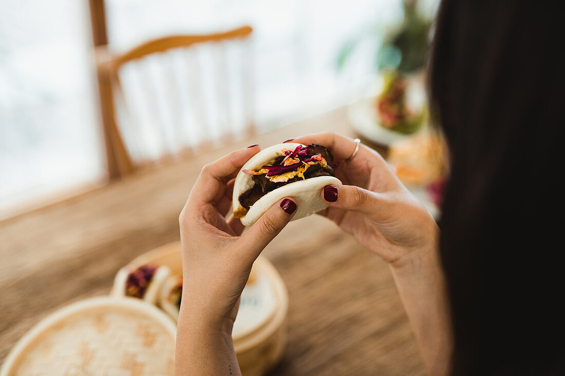 Hands of woman holding traditional Asian sandwich steamed bun with meat and vegetables