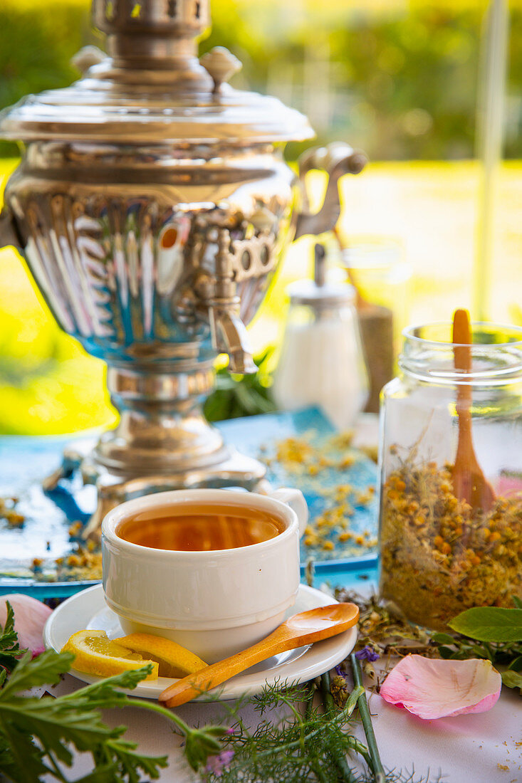 Tasse Tee, Kräuterteemischung und Samowar auf Tisch im Freien