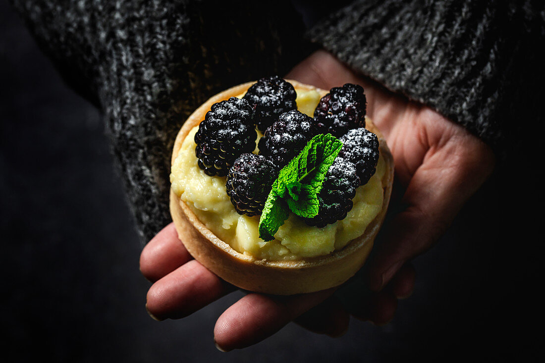 Person hands holding a homemade small cake with blackberry and delicious cream of vanilla and mint