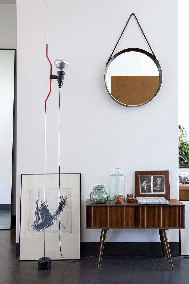 Round mirror above retro sideboard with vintage-style accessories