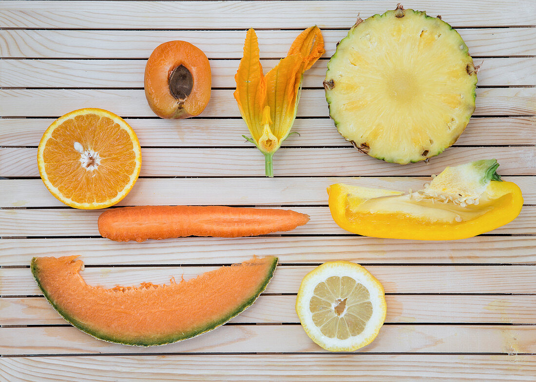 Flatlay of orange and yellow fruits and vegetables arranged on a wooden background