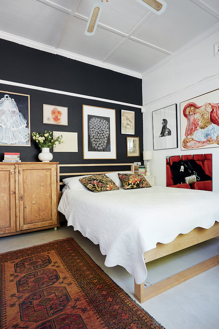 Wooden bed and gallery of pictures on black and white walls in bedroom
