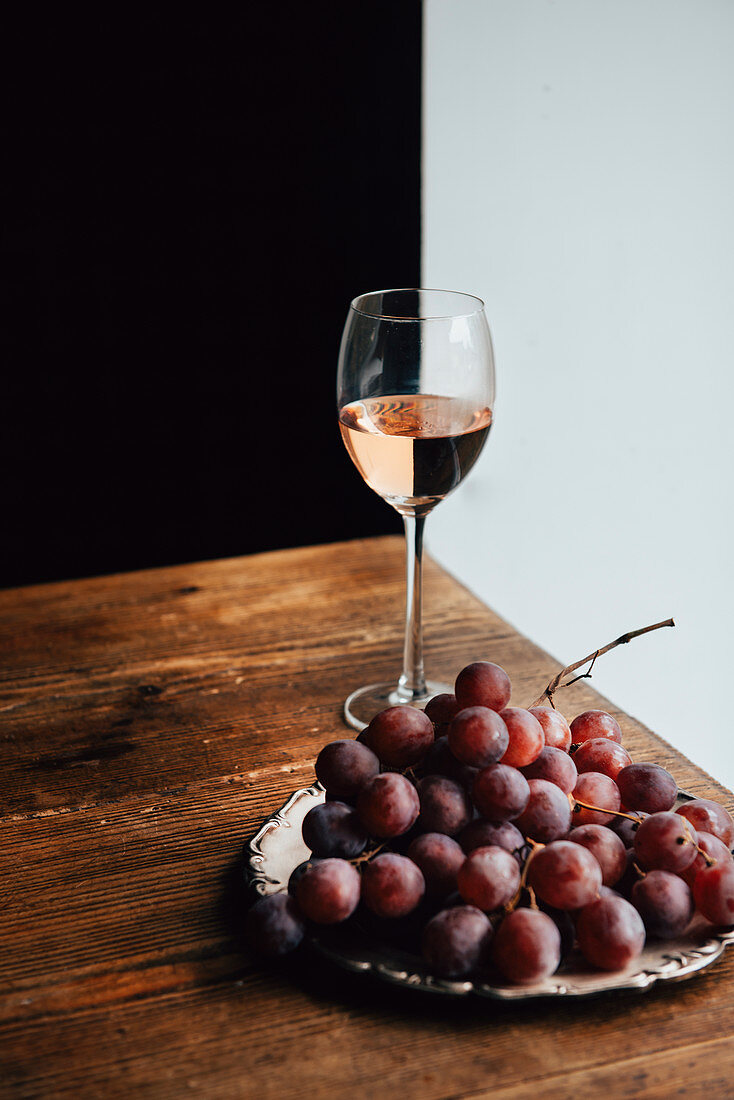 Rote Trauben und ein Glas Rosewein auf Holztisch