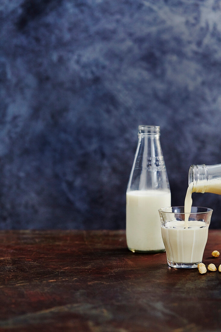 Haselnussdrink aus Flasche in Glas giessen