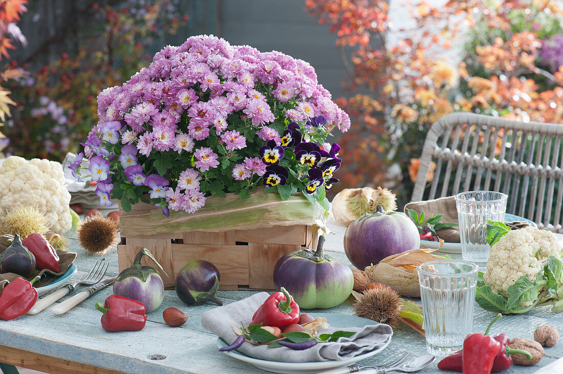 Table decoration with chrysanthemum and horned violets in a woven basket, eggplant, bell pepper, cauliflower, chestnut, chili, and corn