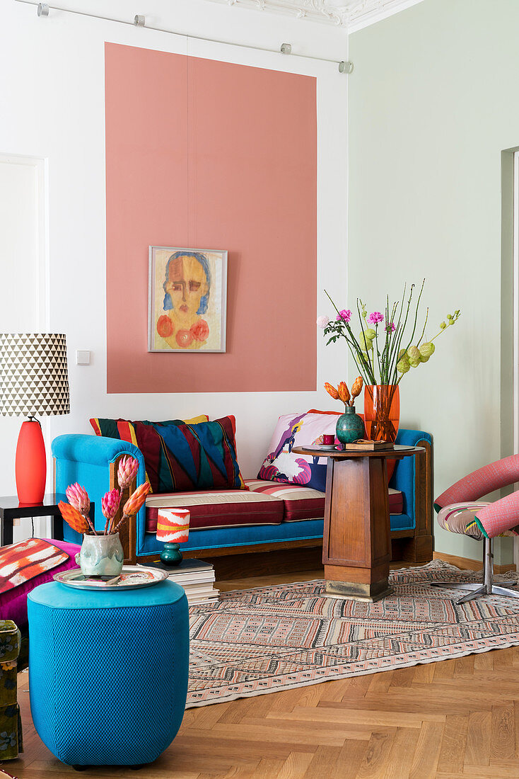 Pouffe and couch providing accents of blue, wooden table and pink field on wall in living room