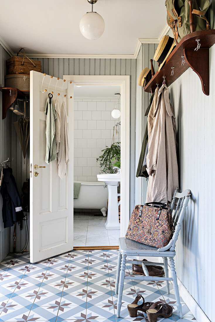 Chair below wall-mounted coat rack in hall with tiled floor and view into bathroom