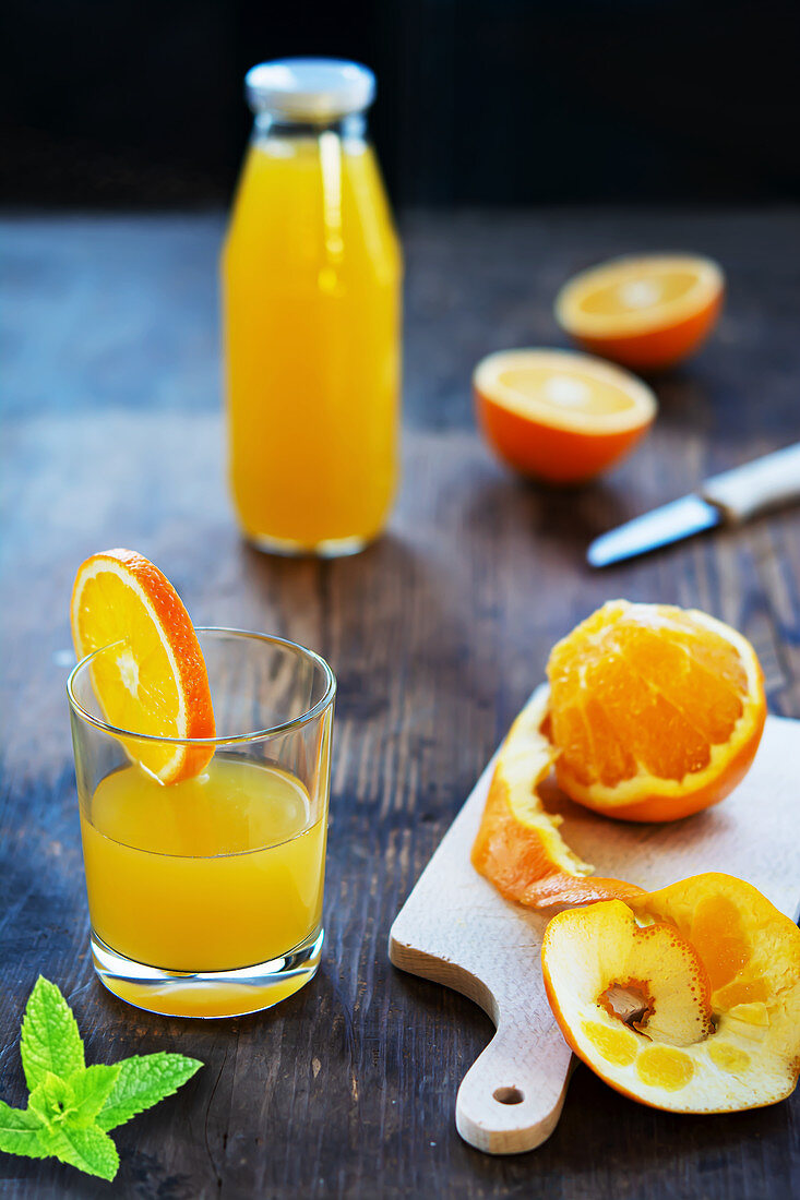 Orangensaft in Glas und Flasche mit frischen Orangen und Minzblättchen